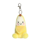 A small yellow banana plush clip-on with rosy cheeks and a friendly smile from Palm Pals by Aurora.