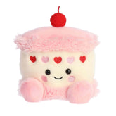 A pink and white layered cake plush topped with small red hearts from the Palm Pals Valentine’s Collection